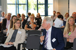 Foto von Prof. Dr. Heinz Günter Holtappels am Mikrophon unter den Teilnehmenden mit Prof. Dr. Nele McElvany