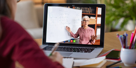 Schülerin sitzt vor ihrem Laptop auf dem ihre Lehrerin per Zoom Unterricht hält