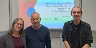 Professorin Nele McElvany, Professor Allan Wigfield und Sebastian Vogel stehen gemeinsam vor der Präsentation