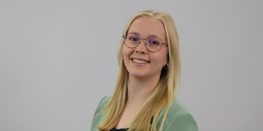Laura Becher lächelt in die Kamera vor einem grauen Hintergrund