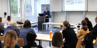 Aileen Edele steht an einem Podium und hält vor einer Gruppe von Menschen ihre Präsentation