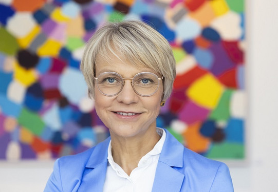 Porträtfoto von Dorothee Feller vor einem bunten Hintergrund