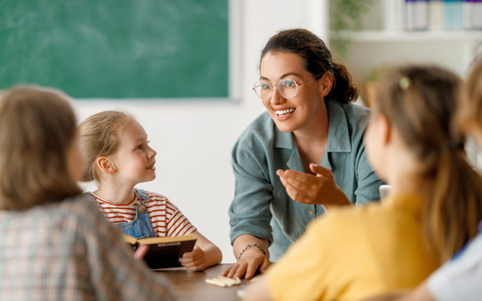 Eine Grundschullehrerin spricht einer Gruppe Kinder im Klassenraum.