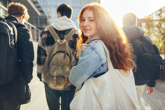 Vier jugendliche Freunde sind auf dem Weg zur Schule. Eine Jugendliche schaut lächelnd nach hinten zur Kamera.