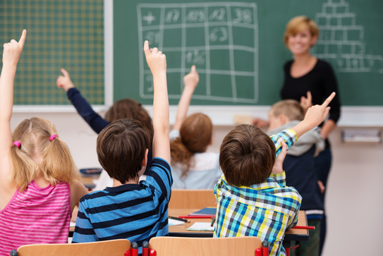 Grundschulkinder, mit dem Rücken zum Betrachter gewandt, melden sich im Unterricht