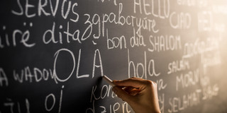 Eine Hand schreibt das Wort Hallo in verschiedenen Sprachen auf eine Schultafel