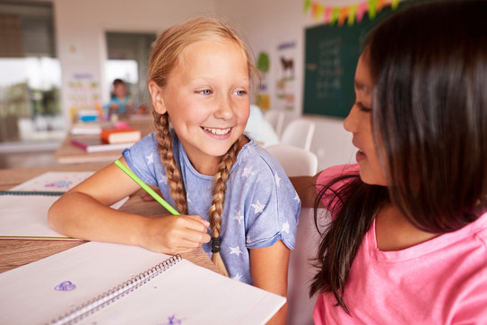 Zwei Schülerinnen sprechen am Schreibtisch miteinander
