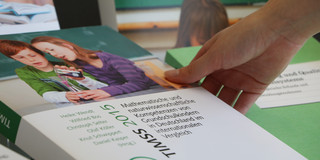 Eine Hand greift nach dem Buch "TIMMS 2015 - Mathematische und naturwissenschaftliche Kompetenzen von Grundschulkindern in Deutschland im internationalen Vergleich"