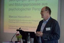 Foto des Plenumvortrags von Prof. Dr. Hasselhorn am Pult mit der Präsentation im Hintergrund