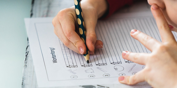 Ein Grundschulkind bearbeitet mit Bleistift ein Übungsblatt.