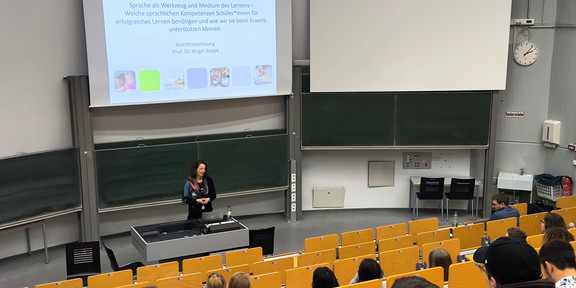 Hörsaal mit mehreren gelben Sitzbänken mit zuhörenden Personen und Prof. Dr. Birgit Heppt am Pult