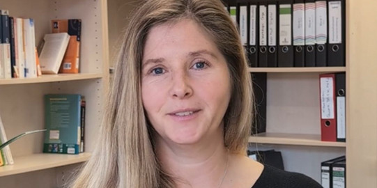 PD Dr. Annika Ohle-Peters steht vor einer Bücherwand im Institut für Schulentwicklungsforschung.