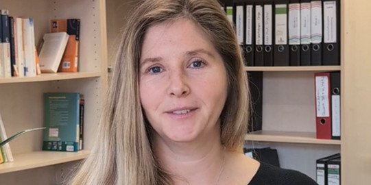 PD Dr. Annika Ohle-Peters steht vor einer Bücherwand im Institut für Schulentwicklungsforschung.