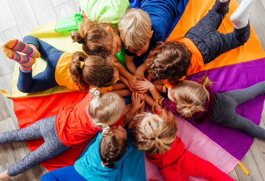 Eine Gruppe aus mehreren Kindern liegen gemeinsam auf einem bunten Spielteppich.