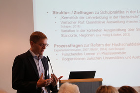 Vortragender Prof. Dr. Johannes König am Pult vor einer Präsentation im Hintergrund