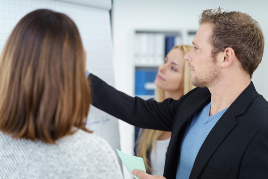 Ein Mann und zwei Frauen stehen vor einem Whiteboard und besprechen sich.
