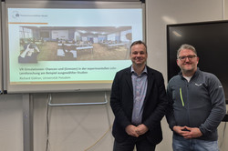 Richard Göllner und Alexander Naumann stehen lächelnd vor der Präsentationsfolie.