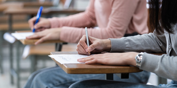 Schulstudie Zwei Schülerinnen sitzen im Klassenraum an ihren Plätzen und schreiben.