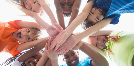 Grundschulkinder stehen im Kreis und halten ihre Hände zusammen