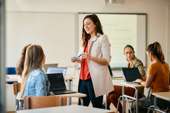 Eine Lehrkraft steht mit älteren Schüler*innen im Klassenraum