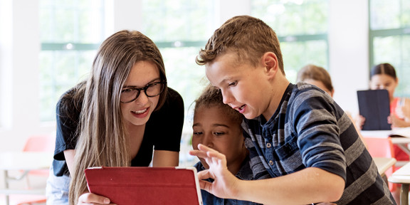 Eine Lehrerin erklärt zwei Schüler*innen etwas am Tablet 