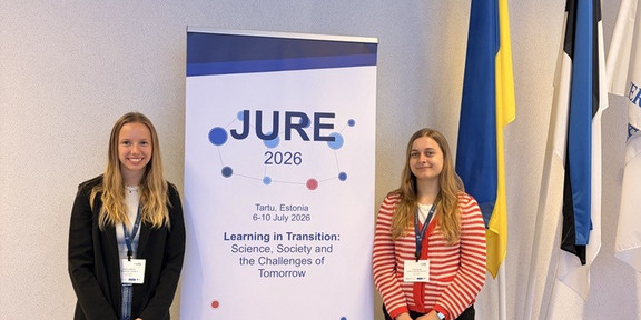 Carina Jüschke und Carina Lohmeier stehen vor einem weißen Aufsteller, der das Logo der Tagung zeigt.