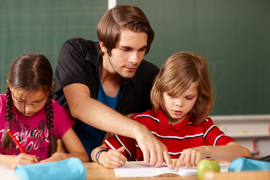 Lehrkraft unterstützt ein Grundschulkind bei einer Aufgabe