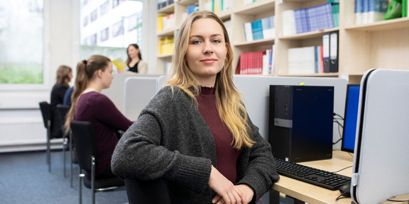 Studierende an PC-Arbeitsplätzen mit Bücherregalen im Hintergrund