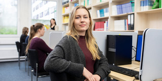 Studierende an PC-Arbeitsplätzen mit Bücherregalen im Hintergrund
