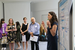 5. Symposium Nachwuchstagung Foto einer Nachwuchswissenschaftlerin bei ihrer Posterpräsentation mit Zuhörenden im Hintergrund