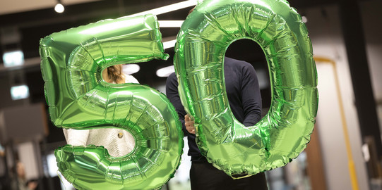 Zwei Personen halten jeweils einen grünen Luftballon, die zusammen die Zahl 50 ergeben.