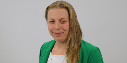 Alyssa Laureen Grecu lächelt vor einem grauen Hintergrund zur Kamera