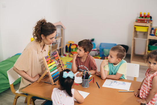 Eine Erzieherin in der Kita zeigt eine Gruppe Kindern ein Rechenbeispiel