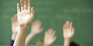 Foto von Kinderhänden, die sich zur Wortmeldung im Unterricht heben