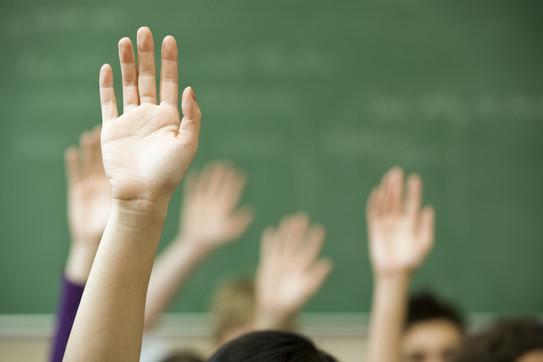 Foto von Kinderhänden, die sich zur Wortmeldung im Unterricht heben