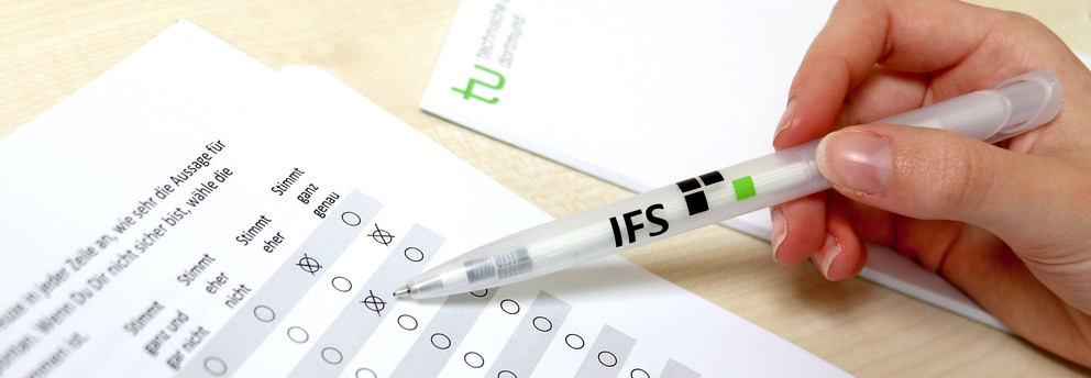 Hand hält IFS-Kugelschreiber und kreuzt Fragebogen an