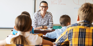Junge Lehrerin sitzt vor einer Schulklasse