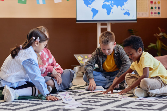 Grundschulkinder spielen am Boden gemeinsam mit ausgedruckten Buchstaben