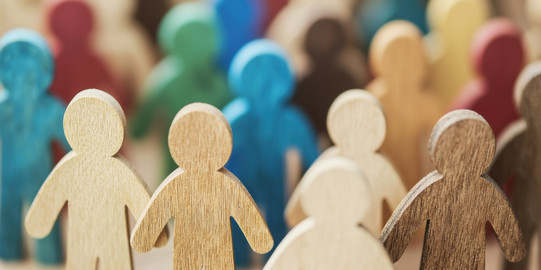 Mehrere menschliche Sihouletten aus bunt bemalten Holz stehen als Gruppe zusammen.