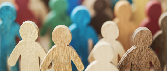 Mehrere menschliche Sihouletten aus bunt bemalten Holz stehen als Gruppe zusammen.