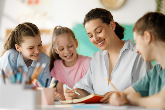 Unterrichten Eine Lehrerin liest drei Schülerinnen aus einem Buch vor.