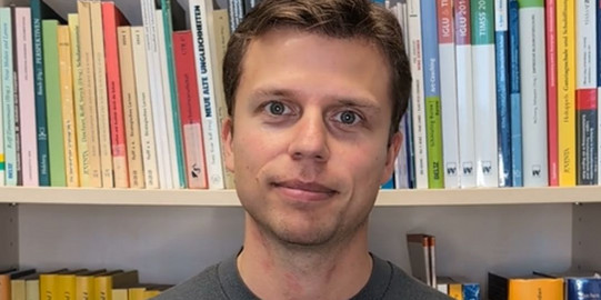 Pascal Alscher steht vor einer Bücherwand im Institut für Schulentwicklungsforschung.