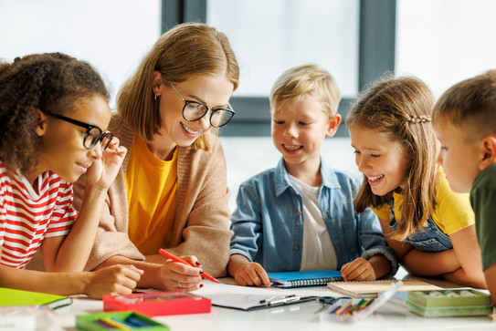 Schulunterricht Schüler*innen und Lehrerin arbeiten in kleiner Gruppe zusammen.