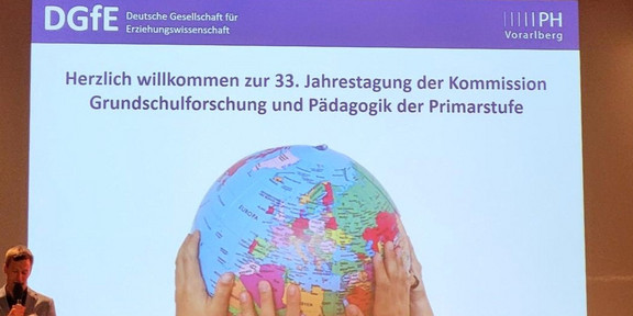 DGfE Präsentation auf der DGfE, auf welcher mehrere Kinderhände einen Globus hochhalten