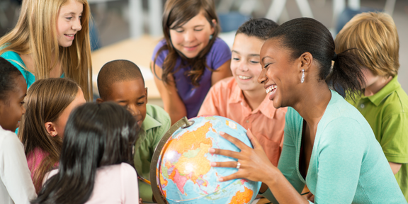 Internationaler Tag der Muttersprache Eine Lehrkraft hält einen Globus und ist von Grundschulkindern umgeben.