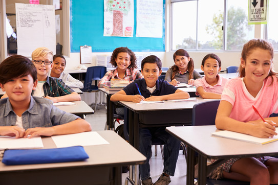 Grundschulkinder sitzen im Klassenraum und lächeln zur Kamera