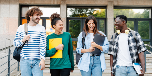 Studierende unterhalten sich im Laufen vor einem Gebäude.