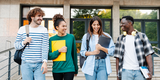 Studierende unterhalten sich im Laufen vor einem Gebäude.