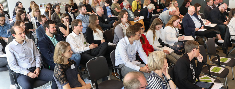 Mehrere Reihen sitzender Menschen, die während eines Symposiums zuhören.